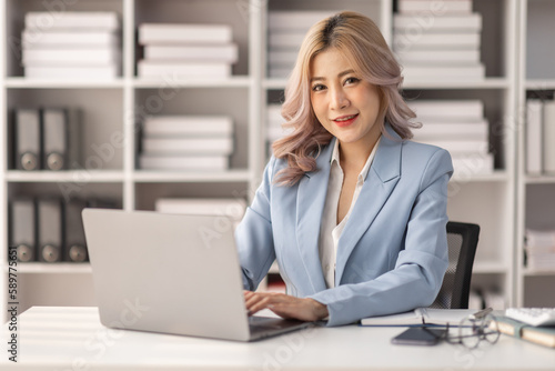Asian Businesswoman Using laptop computer and working at office with calculator document on desk, doing planning analyzing the financial report, business plan investment, finance analysis concept.
