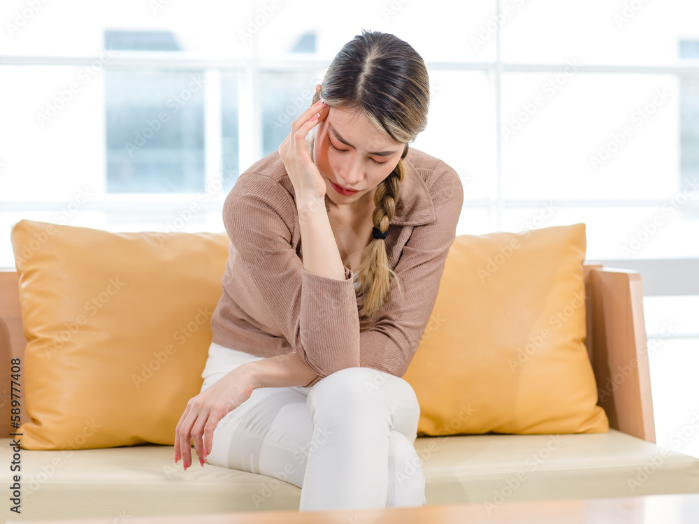 Millennial Asian upset suffered frowning face young female housewife sitting crossed legs on sofa couch in living room at home holding hand headache from office syndrome Millennial Asian upset suffered frowning face young female housewife sitting crossed legs on sofa couch in living room at home holding hand headache from office syndrome