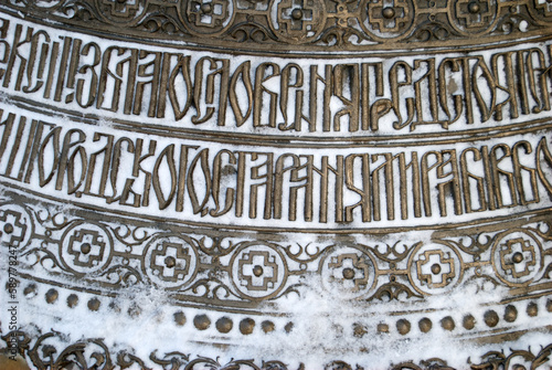 detail of inscription in Cyrillic on a giant gold colored church bell with snow 