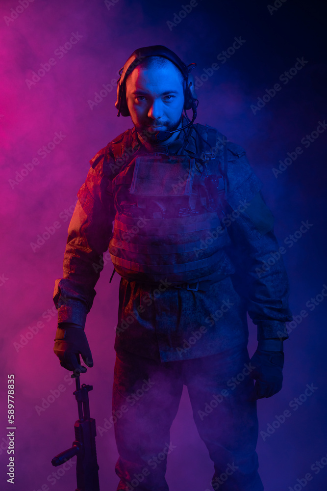 soldier in the studio on a blue background. a man in military uniform with a rifle or machine gun in colored light and smoke. military or airball player. blur