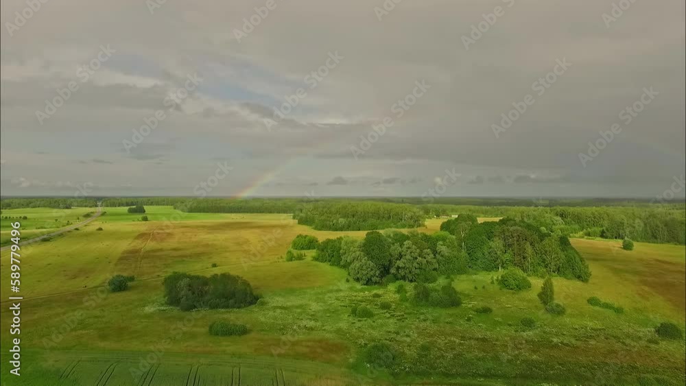 Aerial drone forward moving shot over grasslands along rural countryside with rainbow visible in distance on a cloudy day. Aerial drone forward moving shot over grasslands along rural countryside with rainbow visible in distance on a cloudy day.