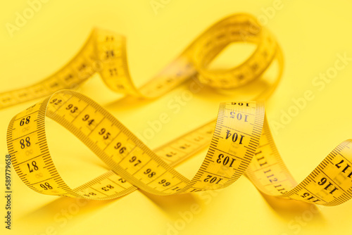 New measuring tape on yellow background, closeup