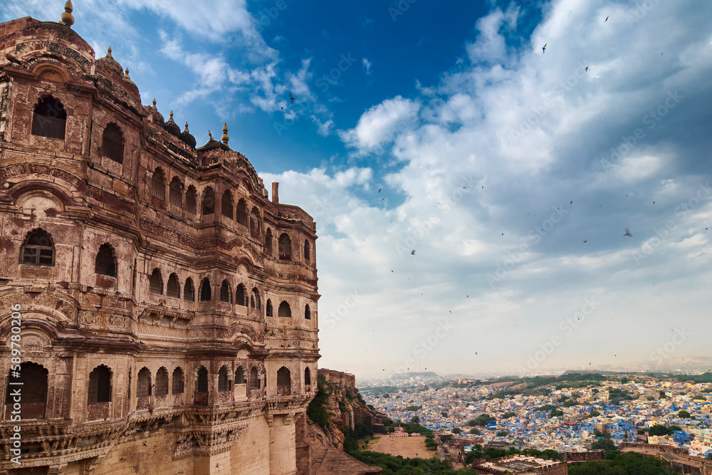 View of Mehrangarh fort with distant view of blue city Jodhpur, Rajasthan, India. Historical Fort is UNESCO world heritage site. Blue sky with white clouds in the background.