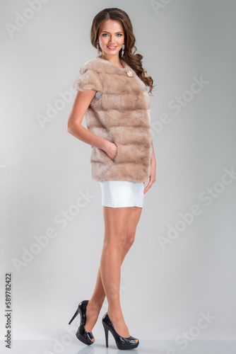 A beautiful young woman of European complexion wearing a fur coat, studio photoshoot