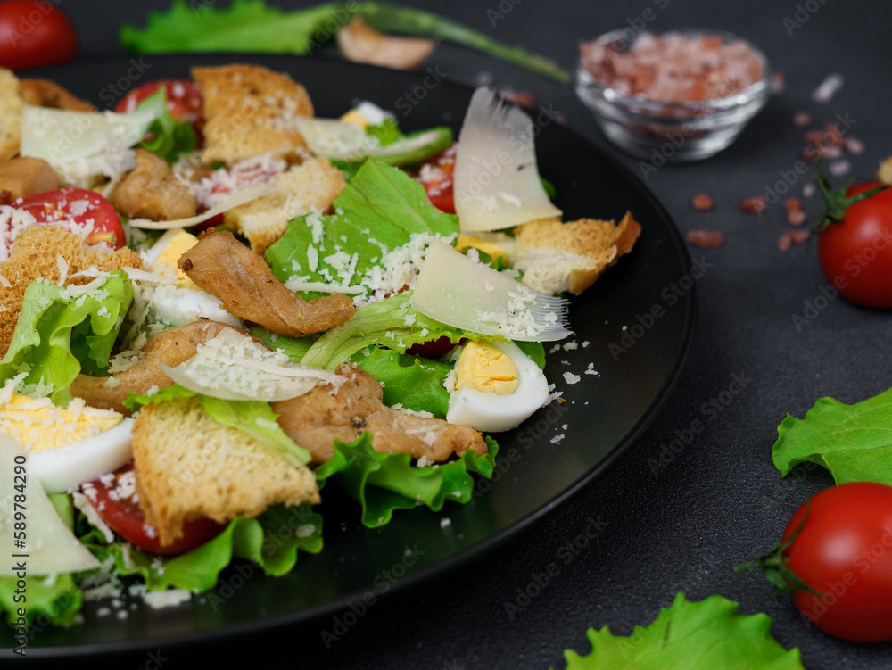 Close-up of a Caesar Salad with chicken, lettuce leaves, cherry tomatoes, grated parmesan in a black plate against a Black Background
Close-up of a Caesar Salad with chicken, lettuce leaves, cherry tomatoes, grated parmesan in a black plate against a Black Background