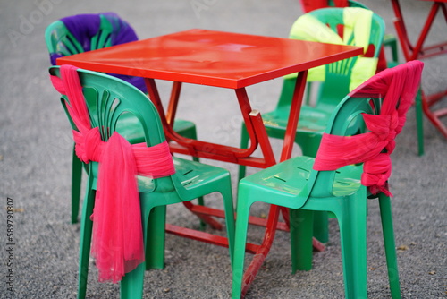 Red table Green plastic chairs tied in green  red  yellow and purple bows