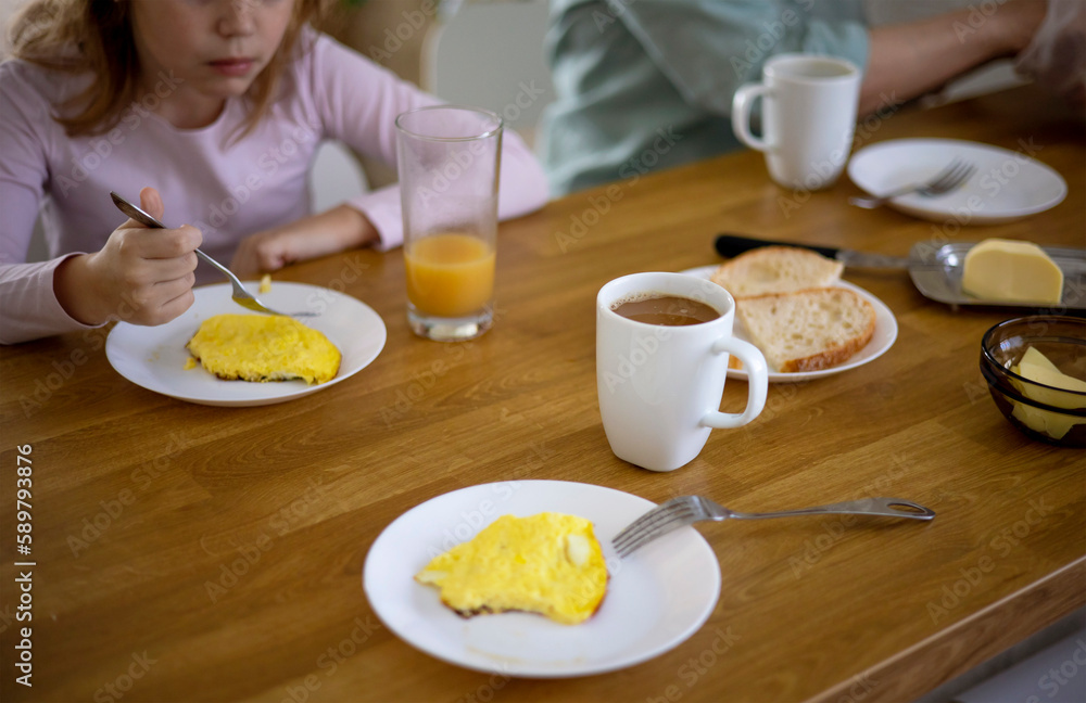 Side view of a family having breakfast in the kitchen with an omelette, a sandwich with butter and cheese, orange juice and coffee. Delicious and healthy breakfast. Selective focus on the coffee mug. Side view of a family having breakfast in the kitchen with an omelette, a sandwich with butter and cheese, orange juice and coffee. Delicious and healthy breakfast. Selective focus on the coffee mug.