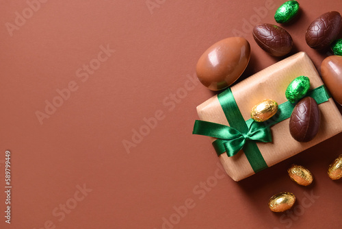Chocolate Easter eggs and gift box with beautiful green bow on brown background
