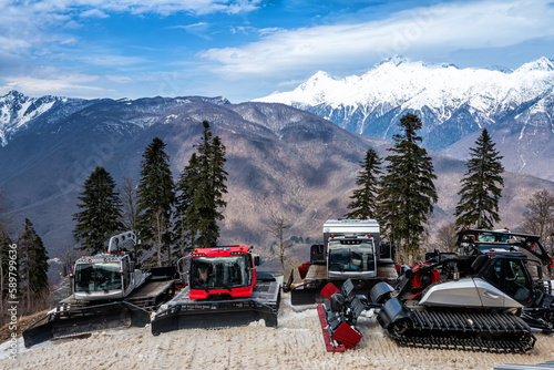 Several snowcats in a picturesque ski resort against the backdrop of beautiful mountains