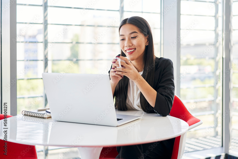 Happy Vietnamese student in modern university using laptop drinking coffee Happy Vietnamese student in modern university using laptop drinking coffee