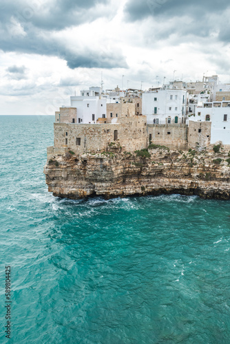 Fototapeta Naklejka Na Ścianę i Meble -  Polignano a Mare, Bari, Italy. Old town built on the rocky cliffs. Traveling concept background with old traditional houses, dramatic cloudy sky and beautiful view of Mediterranean Sea, vertical