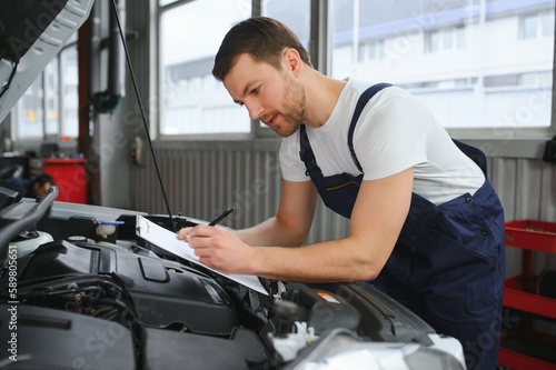 car service, repair, maintenance and people concept - happy smiling auto mechanic man or smith with clipboard at workshop