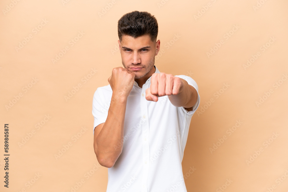 Young caucasian man isolated on beige background with fighting gesture Young caucasian man isolated on beige background with fighting gesture