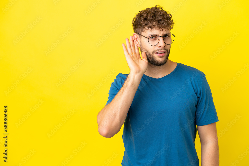 Young handsome caucasian man isolated on yellow background listening to something by putting hand on the ear Young handsome caucasian man isolated on yellow background listening to something by putting hand on the ear