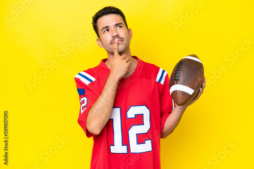 Young handsome man playing rugby over isolated yellow background having doubts while looking up