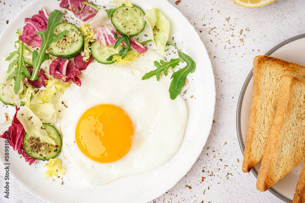 Plate with tasty fried egg, toast and salad on light table Plate with tasty fried egg, toast and salad on light table