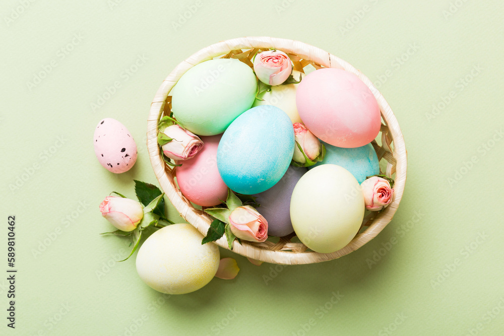 Happy Easter. Easter eggs in basket on colored table with yellow roses. Natural dyed colorful eggs background top view with copy space