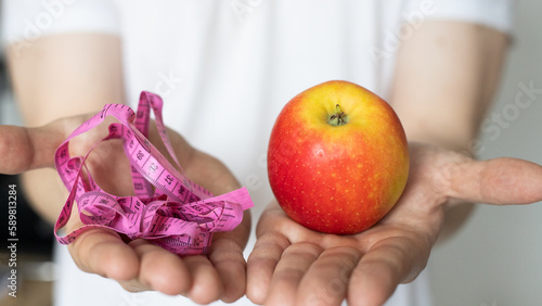 A man in his hands holds a glass of water and a red apple with a measuring tape. The concept of proper nutrition and a healthy lifestyle
