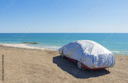 Car covered with reflective cover to protect against sun and dust during a summer trip along the seashore.