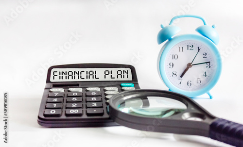 Calculator with the text FINANCIAL PLAN on a white background, next to it is a magnifying glass. Financial concept.