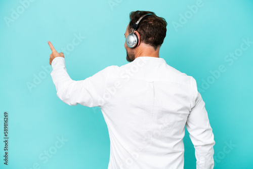 Telemarketer caucasian man working with a headset isolated on blue background pointing back with the index finger