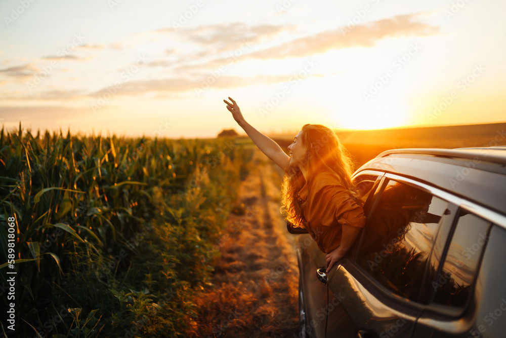 Young happy woman leaning out of the car window enjoying the sunset. The concept of active lifestyle, travel, tourism, nature.