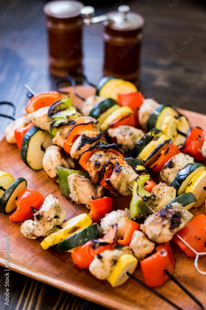 Vertical shot of grilled vegetable and chicken kabobs on a wooden plate Vertical shot of grilled vegetable and chicken kabobs on a wooden plate
