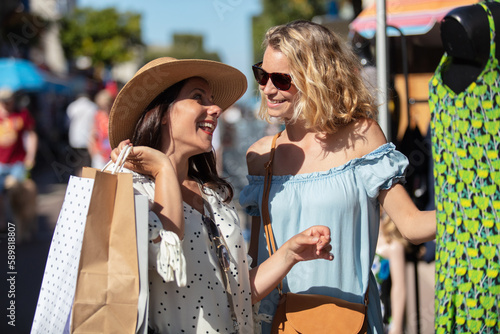 two female friends looking at clothes on summer street market
