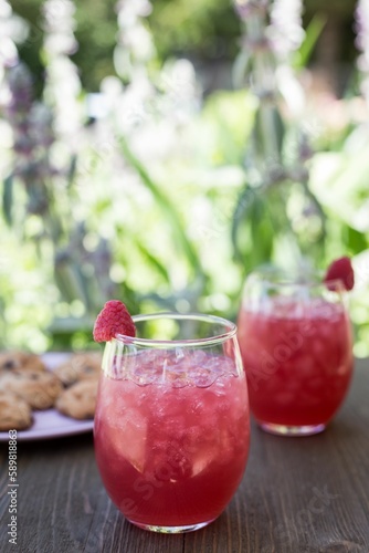 Closeup of red strawberry lemonades with ice put on the table with cookies on blurred background