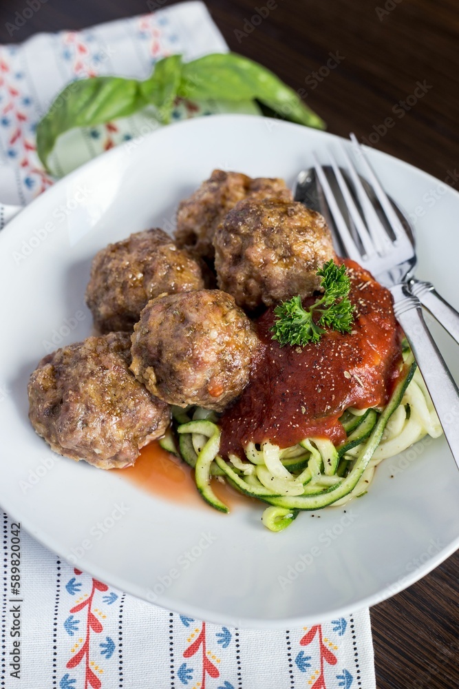Vertical closeup shot of the meatballs with tomato sauce and zoodles on a white plate