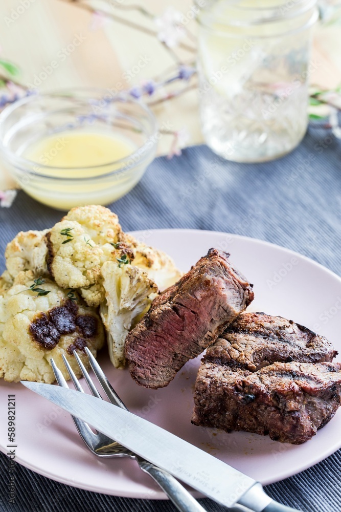 Vertical closeup shot of the steak dinner on a white plate with a sauce and a glass of water Vertical closeup shot of the steak dinner on a white plate with a sauce and a glass of water
