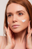 Beautiful young fresh redhead scandinavian woman with cream on face skin in studio. Beauty and skin care