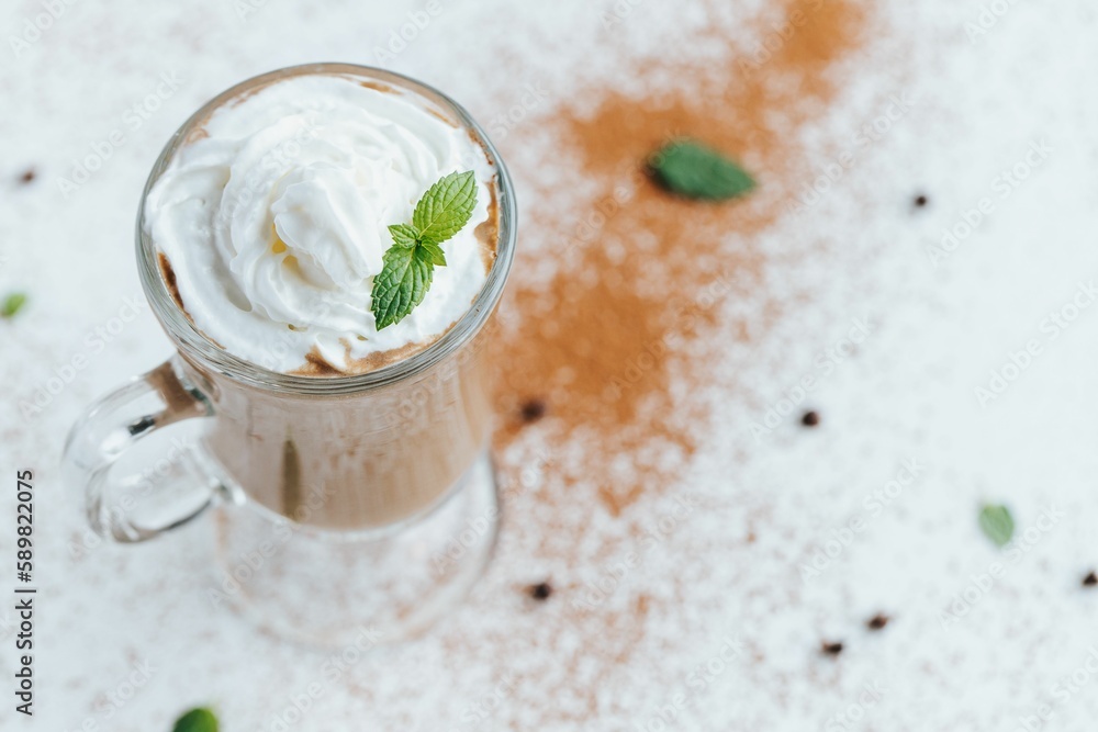 Closeup shot of an iced coffee topped with whipped cream and mint leaves surrounded by cocoa powder Closeup shot of an iced coffee topped with whipped cream and mint leaves surrounded by cocoa powder