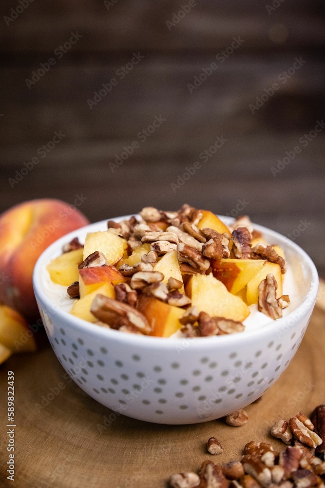 Closeup shot of a bowl of yogurt topped with peaches and walnuts on a wooden board