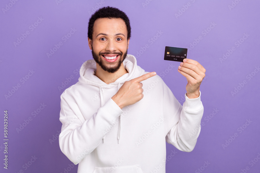 Portrait of handsome guy indicate finger arm hold plastic debit card isolated on purple color background