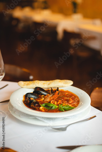 Appetizing Italian soup with seafood in a large white plate. Shrimps, mussels, octopuses. Restaurant serving food.