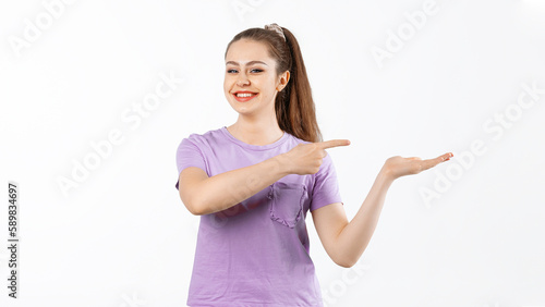 Smiling young woman with long hair points finger at banner, shows great promo offer aside, stands in casual t shirt over white background
