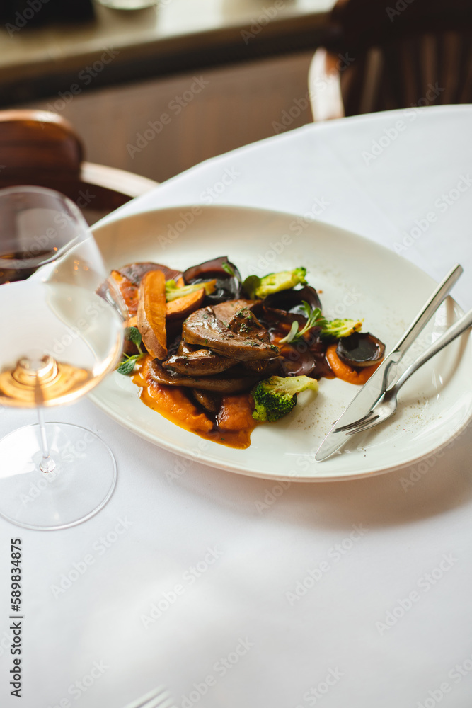 Grilled vegetables in a large white plate. A glass of rose wine on a light background.
