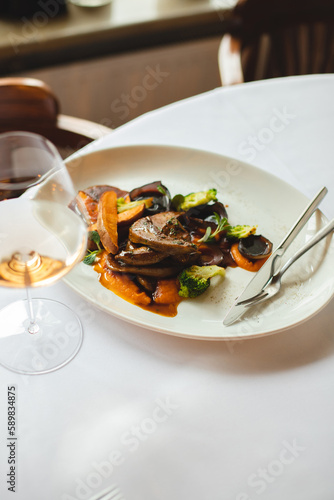 Grilled vegetables in a large white plate. A glass of rose wine on a light background.