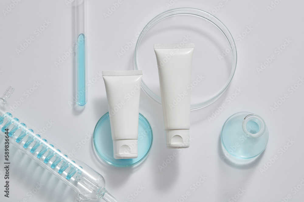 Laboratory concept with test tubes, petri dish and an erlenmeyer flask filled with blue fluid, displayed with empty label tube. Cosmetic packaging mockup