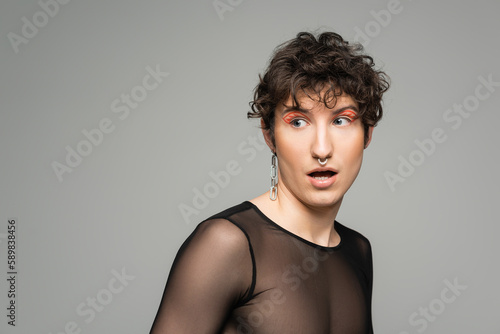 surprised bigender person in black transparent top looking away isolated on grey.