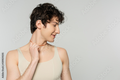 profile of curly bigender model in tank top touching colorful beads isolated on grey.