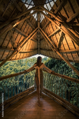 Vertical shot of a female posing leaning on a fence on a balcony with a wooden roof with nature