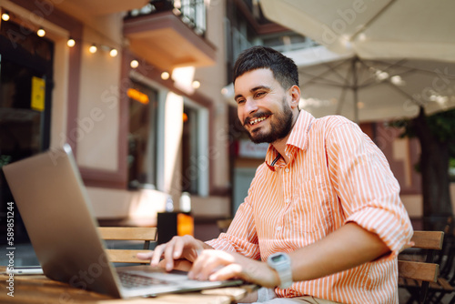 Smiling young man working in a cafe on the street with a laptop and phone. Freelance business concept. Business, blogging, freelancing, education concept. Modern lifestyle.