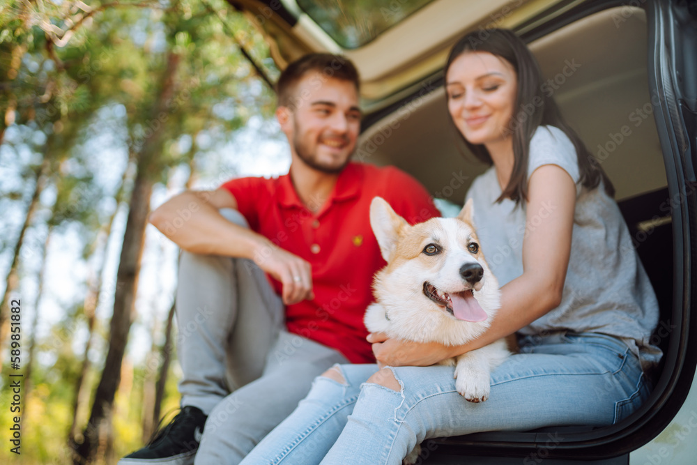 Lovely young couple with a dog sits in the back seat of a car. Happy man with a woman and his beloved dog travel together. Concept of active lifestyle, travel, weekend, relax. Lovely young couple with a dog sits in the back seat of a car. Happy man with a woman and his beloved dog travel together. Concept of active lifestyle, travel, weekend, relax.