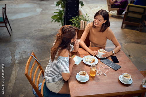 Young beautiful girlfriends having coffee at cafe. Chatting with each other and laughing. photo