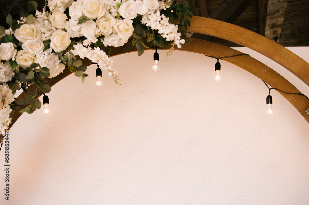 Round wooden arch with white background and decorated with flowers and retro garland