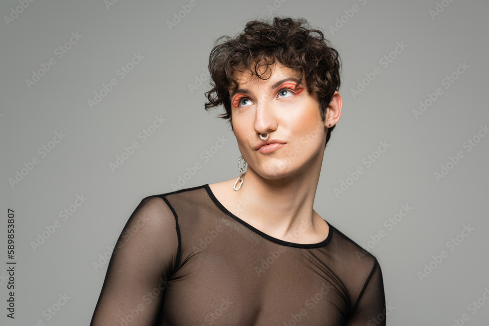 trendy and dreamy pangender person with makeup looking away isolated on grey. trendy and dreamy pangender person with makeup looking away isolated on grey.