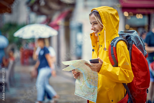 Woman with a yellow raincoat and map on the street while enjoying a walk through the city on a rainy day.