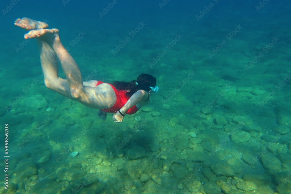 Girl in the red swim suit in the sea. Girl swimming underwater in the ocean. Summer vacation, underwater picture from the snorkeling.